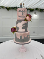 A three-tier fondant covered wedding cake with travel-themed decorations, such as a map and travel suitcase details, and fresh flower decorations.