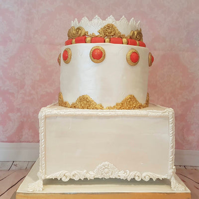 Traditional African wedding cake with one round cake on a floating square cake. It has gold decorations with orange and gold beading details.