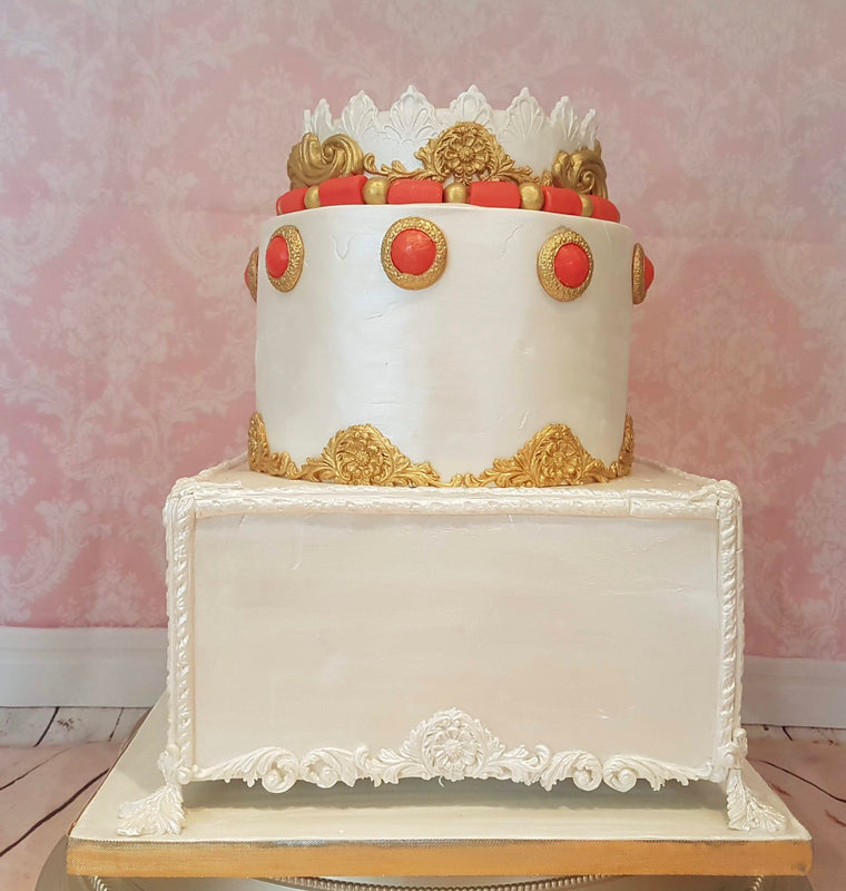 Traditional African wedding cake with one round cake on a floating square cake. It has gold decorations with orange and gold beading details.