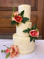 A three-tiered wedding cake with buttercream frosting, decorated with fresh floral decorations.