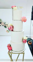 A four-tier fondant covered wedding cake with fresh flower decorations in pink and white colors on each tier.