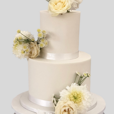 A two-tier fondant wedding cake with white icing and decorated with fresh flowers.