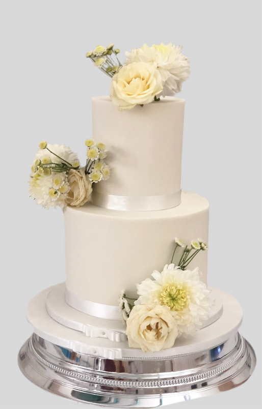 A two-tier fondant wedding cake with white icing and decorated with fresh flowers.