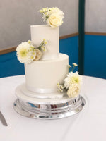 A two-tier fondant wedding cake with white icing and decorated with fresh flowers.