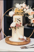 A wedding cake decorated with buttercream and floral hoop stand. The top tier has a personalised topper and a gold acrylic monogram