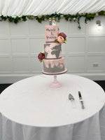 A three-tier fondant covered wedding cake with travel-themed decorations, such as a map and travel suitcase details, and fresh flower decorations.