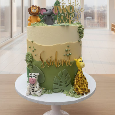 Decorative cake with animal figures and greenery on a white surface