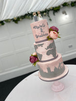 A three-tier fondant covered wedding cake with travel-themed decorations, such as a map and travel suitcase details, and fresh flower decorations.