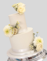 A two-tier fondant wedding cake with white icing and decorated with fresh flowers.