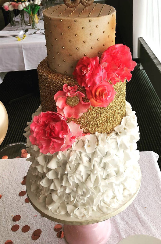 A three-tiered wedding cake with a combination of white fondant ruffles and golden tiers, decorated with pink sugar flowers.