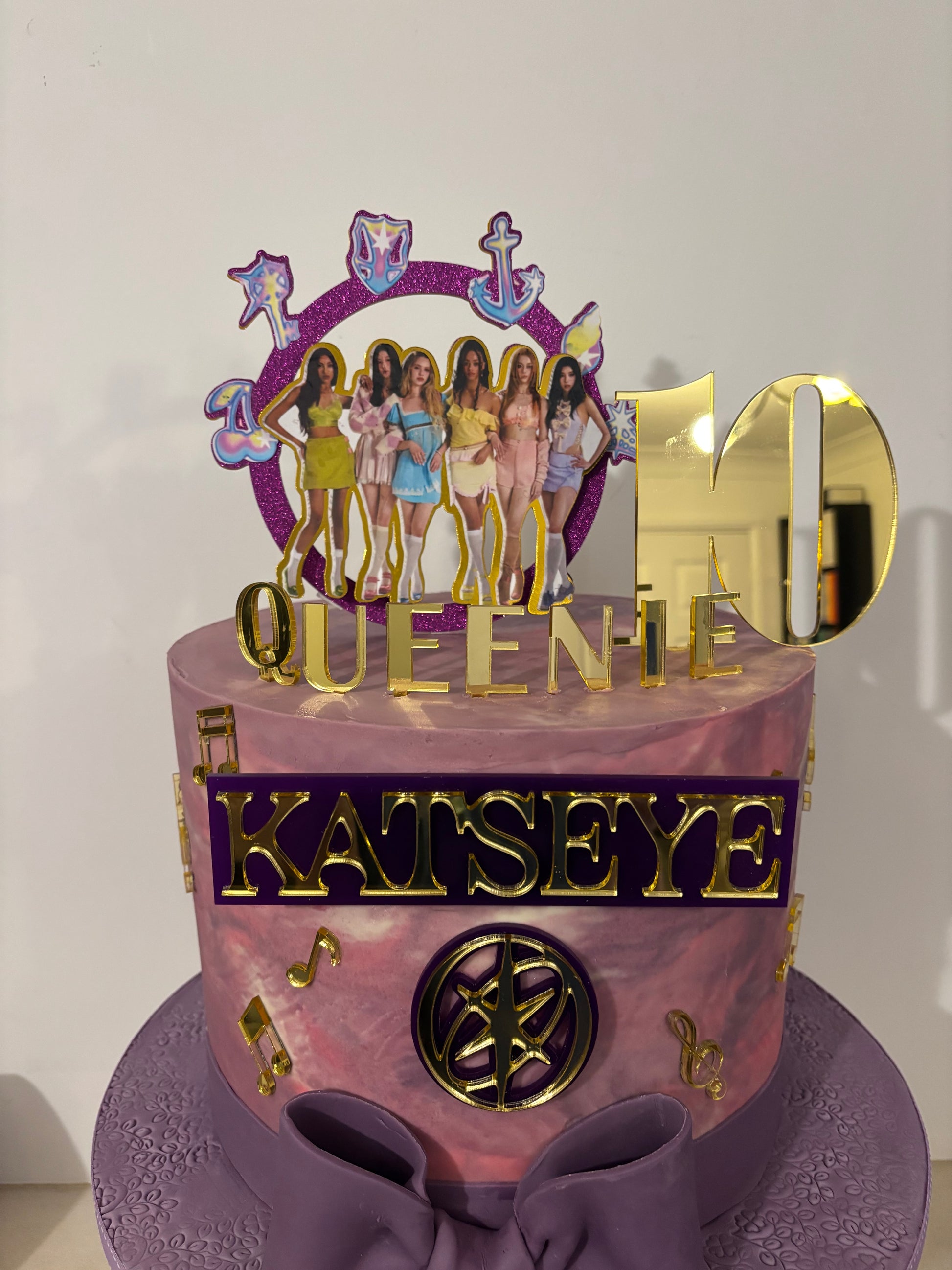 Decorative cake with ‘Katseye' text, featuring a purple and gold design.