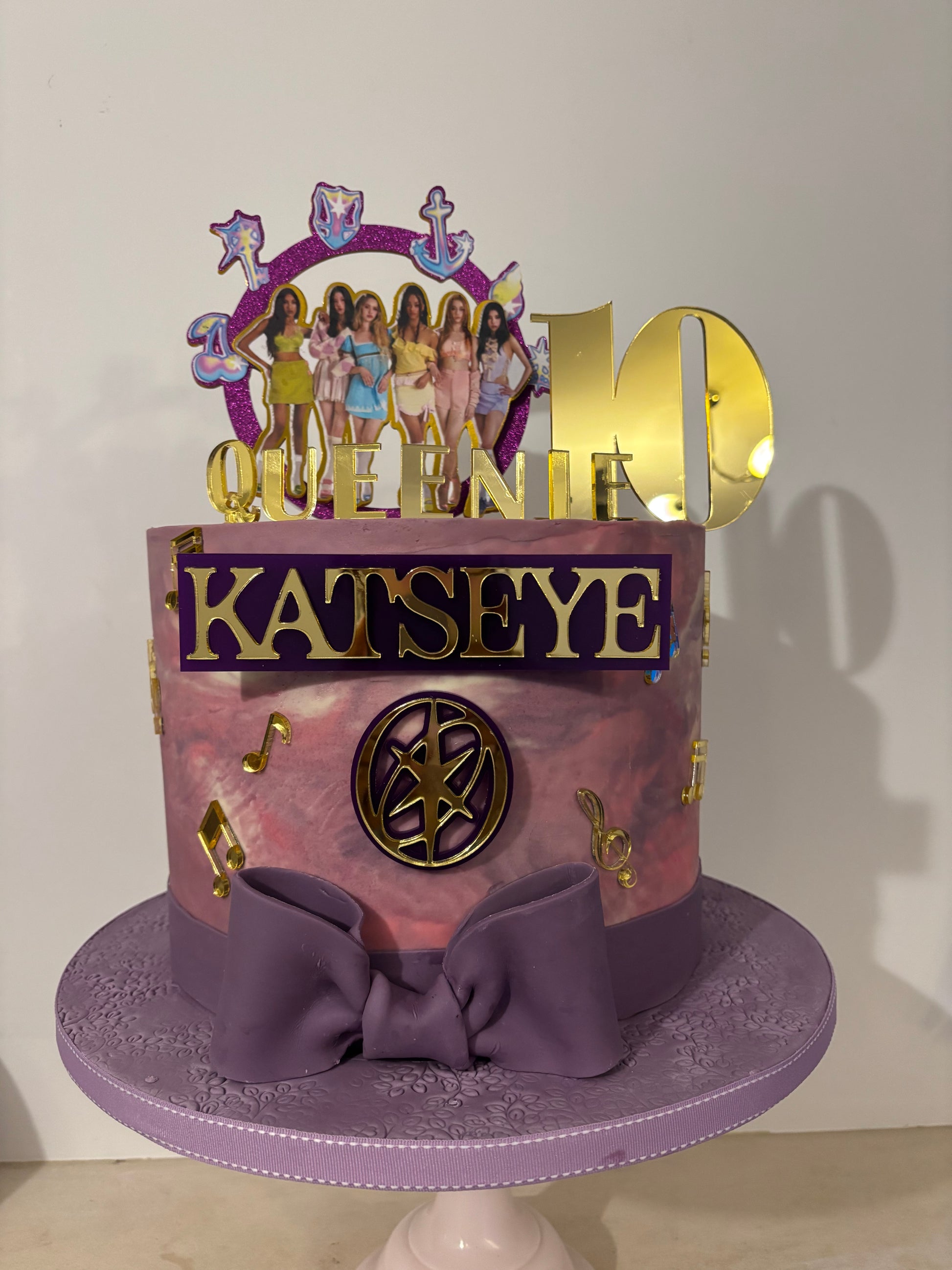 Purple cake with decorative elements and 'Katseye' branding on a white background