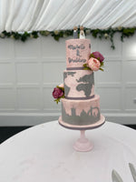A three-tier fondant covered wedding cake with travel-themed decorations, such as a map and travel suitcase details, and fresh flower decorations.